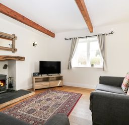A living room with a wood burning stove tv on a wooden stand patterned rug and gray sofas at Glen Cottage in Troutbeck near Keswick