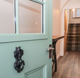 A hallway with a mint green door opening to a wooden floor and stairs with plaid carpet at Oak Cottage in Windermere