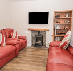 A living room with red leather sofas a wall-mounted TV a fireplace and a wooden shelving unit at Oak Cottage in Windermere