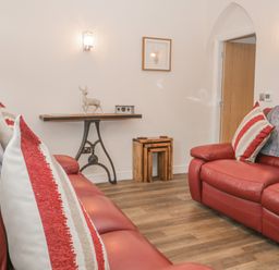 A living room with red leather sofas striped cushions wooden floor table with a metal base and a deer statue at Oak Cottage in Windermere