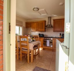 A kitchen with wooden cabinets and a dining table set with plates and wine bottles at Barcud Cottage Golden Grove near Llandeilo
