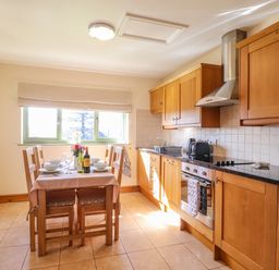 A kitchen with wooden cabinets a dining table set for four and kitchen appliances at Barcud Cottage in Golden Grove near Llandeilo