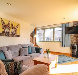 A living room with a grey sofa cushions a wooden coffee table and a mounted TV at Barcud Cottage in Golden Grove near Llandeilo