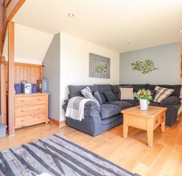 A living room with a gray sectional sofa a wooden coffee table with flowers a striped rug wooden stairs and a wooden cabinet at Gwennol Cottage Golden Grove near Llandeilo