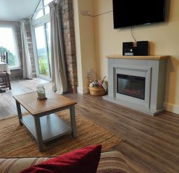 A living room with a coffee table a fireplace a wall-mounted television and glass doors at Sewin Cottage Golden Grove near Llandeilo
