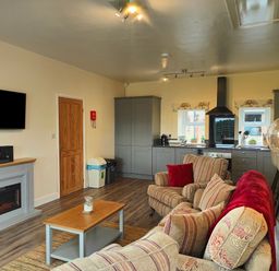 A living room and kitchen area with sofas a coffee table a wall-mounted TV and grey kitchen cabinets at Sewin Cottage in Golden Grove near Llandeilo