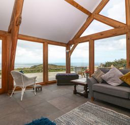 A living room with large wooden framed windows and a gray sofa with pillows at Balog Farm in Amlwch