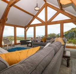 A living room with large windows wooden beams gray sofas and pillows at Balog Farm in Amlwch