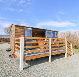 A small wooden cabin with a raised deck and outdoor furniture on a gravel area at Elan in Rhayader