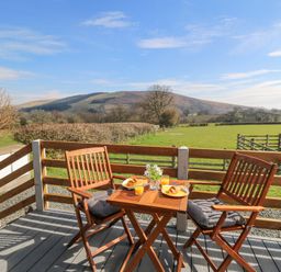 A wooden patio table with two chairs and breakfast setting overlooking a green field and hills at Elan in Rhayader