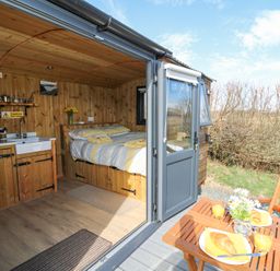 A small wooden cabin with a bed and kitchen area next to a patio with a table set for breakfast at Elan in Rhayader