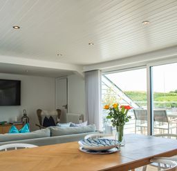 A dining table with a vase of flowers and plates next to a sofa and a large window with a balcony view at The Penthouse in Salcombe