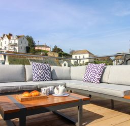 An outdoor sofa with pillows and a table set with a teapot and croissants at The Penthouse in Salcombe