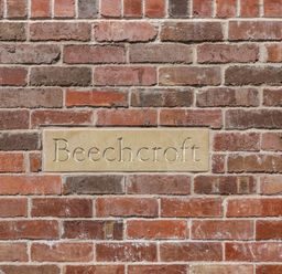 A brick wall with a rectangular stone plaque engraved with the word Beechcroft