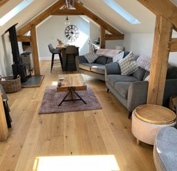 An attic living room with wooden beams two sofas a coffee table a wood burning stove a dining table with chairs and skylights at Lugg View Cross Keys near Hereford