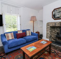 A living room with a blue sofa, wooden table, and a fireplace at Dolwylan Cottage in Cwmtydu near New Quay
