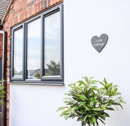 A white wall with a black heart-shaped sign saying Little Oakleigh next to a window and plants in pots at Oakleigh in Four Crosses