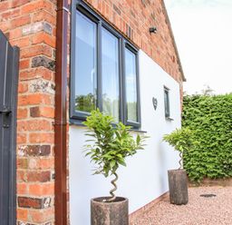 Exterior of a brick and white wall building with black window frames two potted plants gravel ground and a green hedge at Oakleigh in Four Crosses