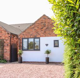 A brick and white exterior wall with two windows and two potted plants on gravel at Oakleigh in Four Crosses