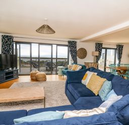 A living room with blue sofas pillows a coffee table TV and sliding glass doors opening to a balcony at Ty Ni in New Quay