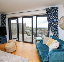 A living room with a blue sofa pillows large clock sliding glass doors and balcony at Ty Ni in New Quay