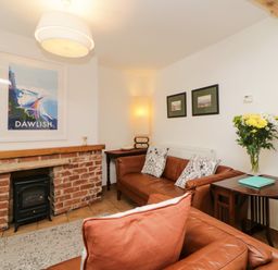 A sitting room with a brick fireplace brown leather sofas and a side table with flowers at The Yellow House 13 King Street in Dawlish