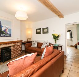 A living room with two brown leather sofas a brick fireplace with a small black stove a wooden side table with flowers and framed pictures on the wall at The Yellow House 13 King Street in Dawlish
