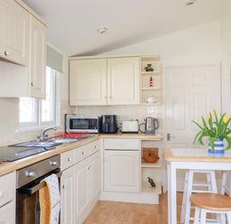 A kitchen with cream cabinets a wooden countertop appliances and a table with yellow flowers at 224 Atlantic Bays in St Merryn
