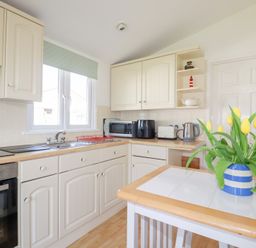 A kitchen with cream cabinets a sink a microwave toaster kettle and yellow flowers in a striped vase on a table at 224 Atlantic Bays in St Merryn