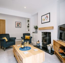 A living room with blue armchairs a wooden coffee table a fireplace and a television at Craig Cottage in Bowness-On-Windermere