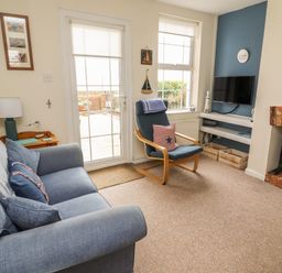A living room with a blue sofa and chair a fireplace and wall-mounted tv at 9 Harefield Cottages in Lympstone
