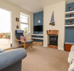 A living room with blue chair a plaid sofa a fireplace and a television at 9 Harefield Cottages in Lympstone