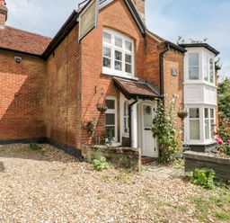 An exterior view of a brick house with white framed windows roses by a stone wall and a gravel driveway at Oakapple Cottage in Swan Green near Lyndhurst