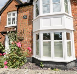 Exterior view of a brick cottage with white bay windows and pink flowers in front at Oakapple Cottage Swan Green near Lyndhurst