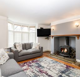 A living room with two grey sofas near a bay window and a fireplace with a wood stove at Oakapple Cottage in Swan Green near Lyndhurst