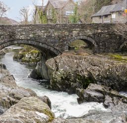 A stone bridge over a river with rocks and buildings in the background at Ty Capel in Betws Y Coed