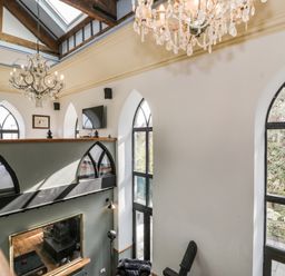 An interior view of a two-story room with arched windows chandeliers a mounted television and wooden beams at Greystones Chapel in Cwm-y-Glo near Llanrug