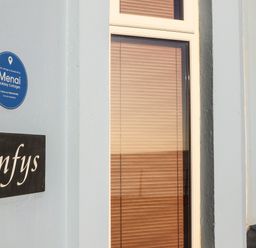 A cottage wall with Enfys nameplate and Mengi Holiday Cottages blue plaque in Criccieth