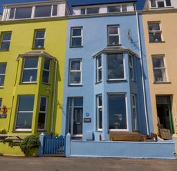 A row of colorful tall houses with bay windows and small fenced front yards at Enfys in Criccieth