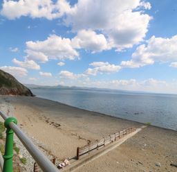 A beach with sand and pebbles and a metal railing along a path at Enfys in Criccieth