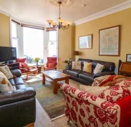 A living room with two black leather sofas a red patterned armchair wooden coffee table and a television by a window at Enfys in Criccieth