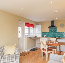 A kitchen and dining area with a table set for tea and a checkered armchair at Roundham Cottage in West Bay