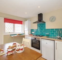 A kitchen with a dining table set with tea cups and muffins and green tiled backsplash at Roundham Cottage in West Bay
