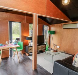 A living area with green chairs a wooden table and a sofa with cushions at The Tractor Shed in Lower Broadheath Worcester