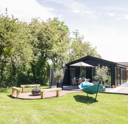 A backyard with wooden benches around a fire pit a green hammock and a black shed with a patio at The Tractor Shed in Lower Broadheath Worcester