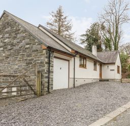 A house with a stone wall garage and a gravel driveway at Bryn Elsi in Betws Y Coed