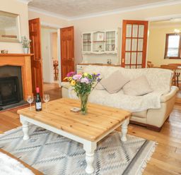 A living room with a wooden coffee table holding a vase of flowers and a bottle of wine and two glasses near a fireplace and sofas at Bryn Elsi in Betws-Y-Coed