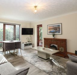 A living room with a brick fireplace a coffee table sofas a dining table with chairs and a wall-mounted television at Seaview Cottage in Salthouse Norfolk