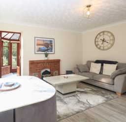 A living room with a gray sofa a marble coffee table a brick fireplace and wall clock at Seaview Cottage in Salthouse Norfolk