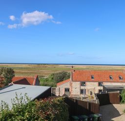 A view of stone cottages with orange roofs overlooking fields and the sea at Seaview Cottage in Salthouse Norfolk